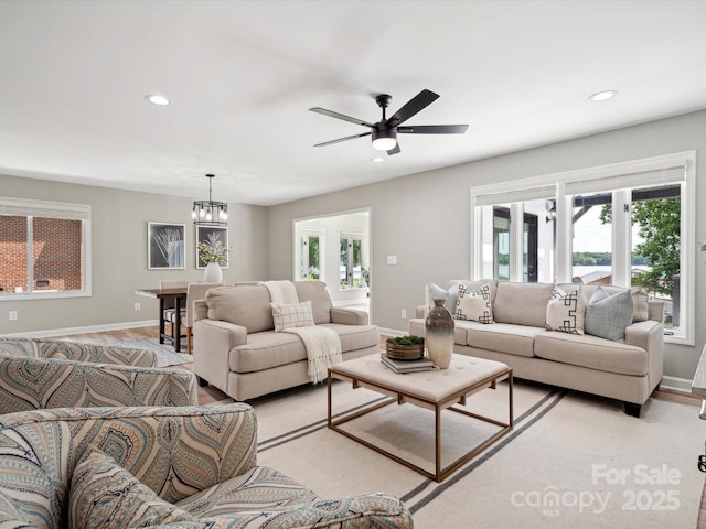 living room featuring ceiling fan with notable chandelier, light wood-style flooring, baseboards, and recessed lighting