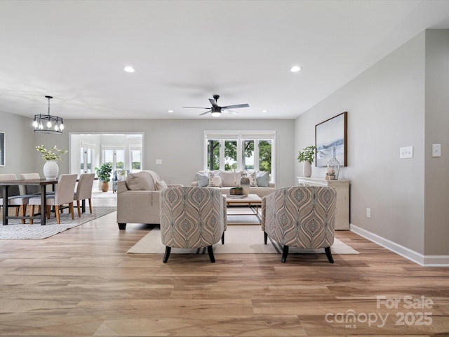 living room with ceiling fan with notable chandelier, baseboards, light wood-style floors, and recessed lighting