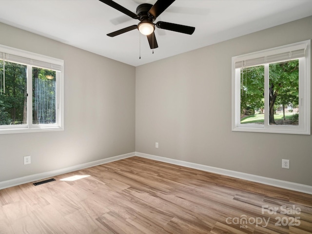spare room featuring wood finished floors, baseboards, ceiling fan, and visible vents