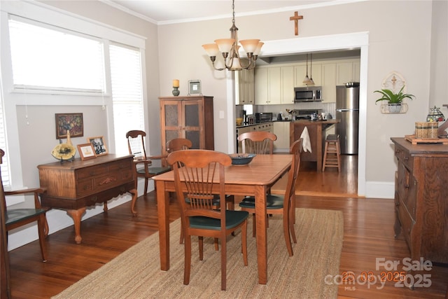 dining space with wood finished floors, crown molding, a notable chandelier, and baseboards