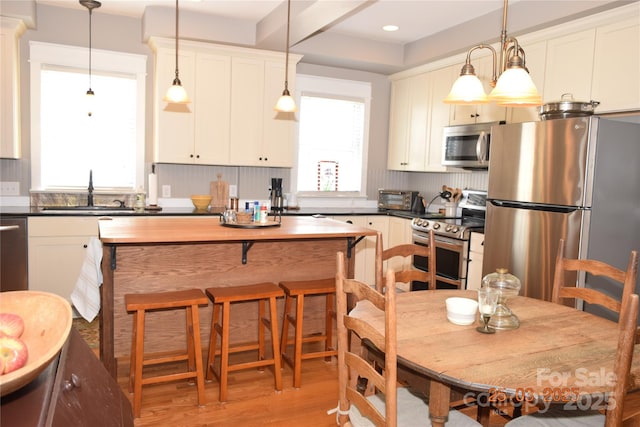 kitchen with pendant lighting, a sink, light wood-style floors, stainless steel appliances, and a toaster