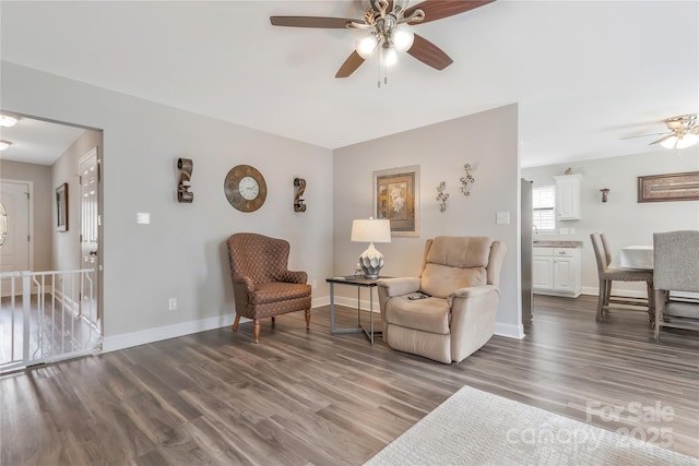 living area with wood finished floors, an upstairs landing, baseboards, and ceiling fan
