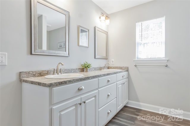 bathroom with baseboards, double vanity, a sink, and wood finished floors