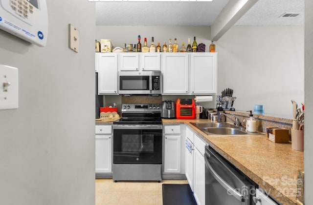 kitchen with appliances with stainless steel finishes, a sink, a textured ceiling, white cabinets, and light countertops