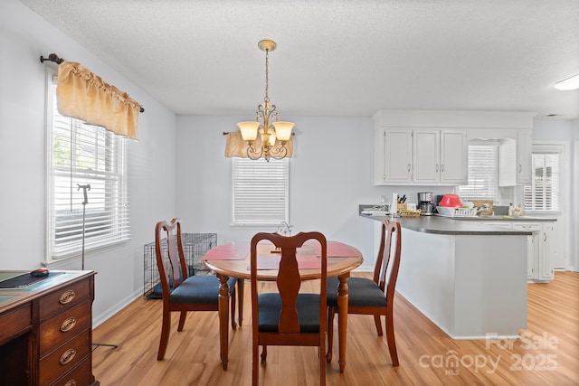 dining area featuring a textured ceiling, light wood-style flooring, and an inviting chandelier
