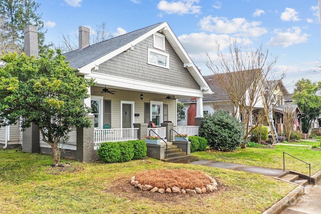 view of front of property featuring a front yard, covered porch, roof with shingles, a ceiling fan, and a chimney