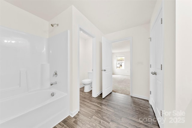 bathroom featuring toilet, baseboards, bathing tub / shower combination, and wood finished floors