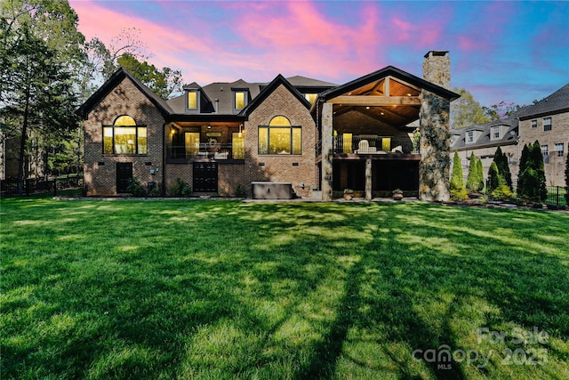 back of property featuring a lawn, a chimney, brick siding, and a balcony