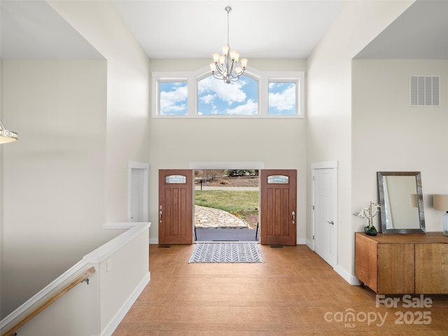 foyer entrance featuring a high ceiling, visible vents, a chandelier, and light wood finished floors