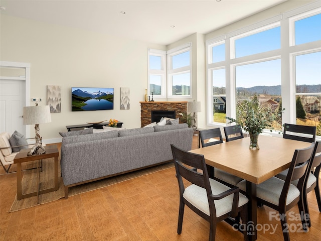 dining space with baseboards, a fireplace, a high ceiling, and light wood-style flooring