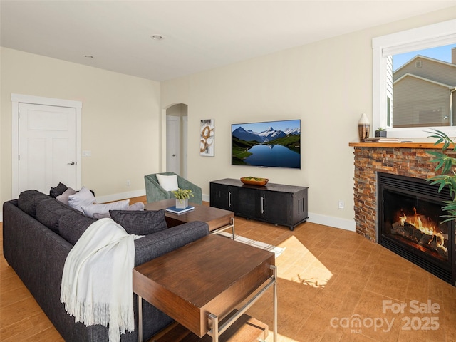 living area with arched walkways, baseboards, and a stone fireplace