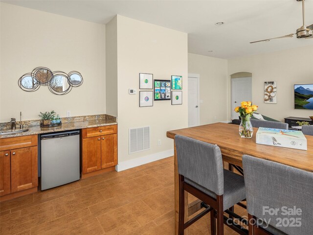 kitchen featuring arched walkways, visible vents, dishwasher, light stone countertops, and brown cabinetry