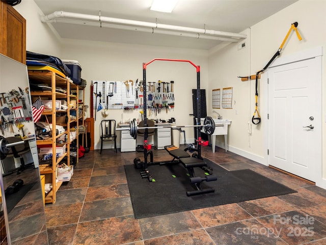 exercise area featuring a workshop area, stone finish floor, and baseboards