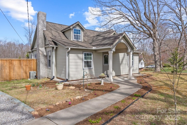 view of front of house with a chimney, a shingled roof, fence, and central AC