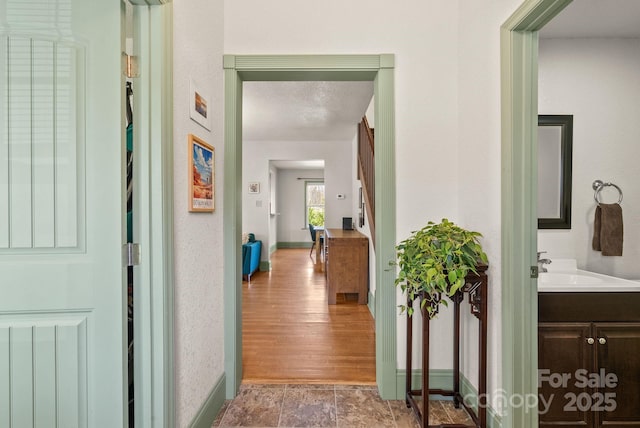 hallway with baseboards, a textured ceiling, and a textured wall