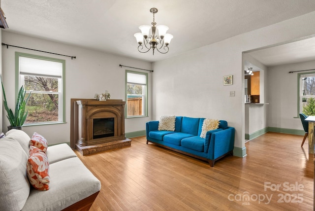 living area with a glass covered fireplace, baseboards, hardwood / wood-style flooring, and a chandelier