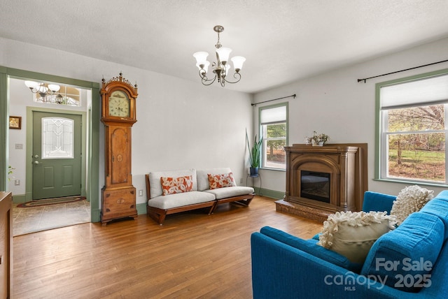 living area with a textured ceiling, wood finished floors, a glass covered fireplace, and a chandelier