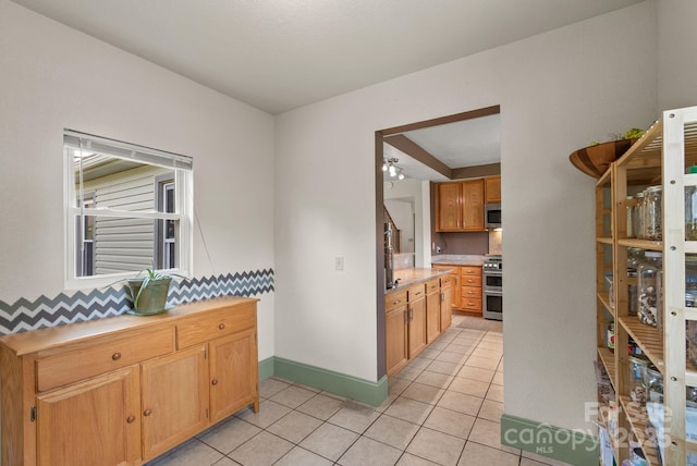 kitchen with light countertops, light tile patterned floors, stainless steel appliances, baseboards, and a ceiling fan