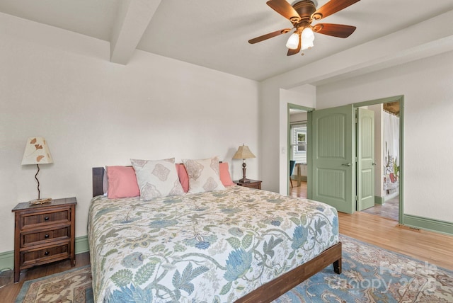bedroom featuring baseboards, wood finished floors, a ceiling fan, and beam ceiling
