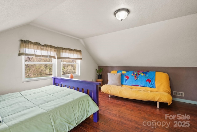 bedroom featuring wood-type flooring, a textured ceiling, vaulted ceiling, and visible vents