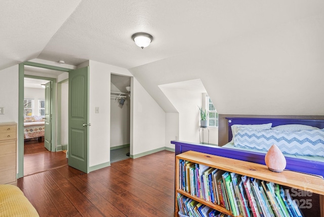 bedroom featuring lofted ceiling, a textured ceiling, wood finished floors, and multiple windows