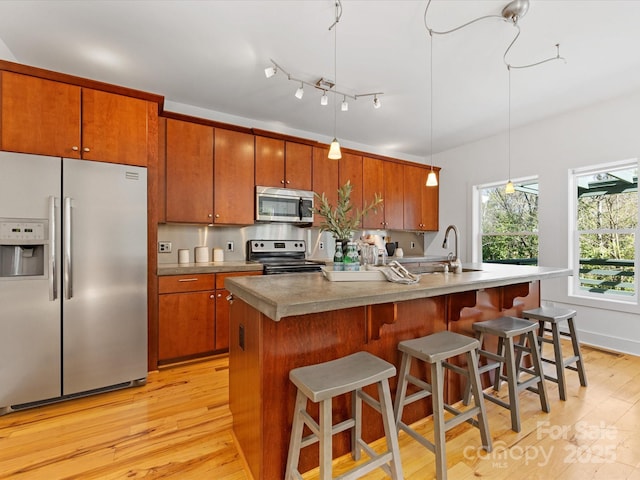 kitchen with light wood-style floors, a kitchen island with sink, brown cabinets, and stainless steel appliances