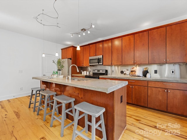kitchen with a kitchen breakfast bar, appliances with stainless steel finishes, a sink, light countertops, and light wood-style flooring