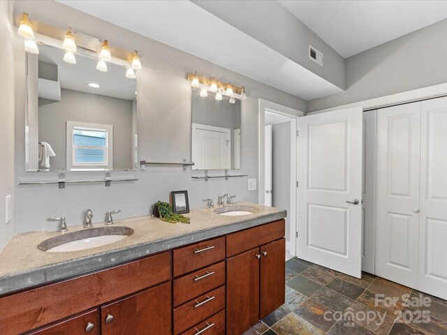 bathroom featuring visible vents, a sink, stone finish floor, and double vanity