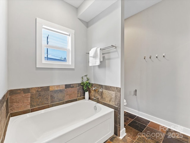 full bathroom with stone finish floor, baseboards, toilet, and a bath