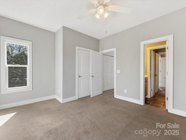 unfurnished bedroom featuring a ceiling fan, baseboards, dark carpet, and ensuite bathroom