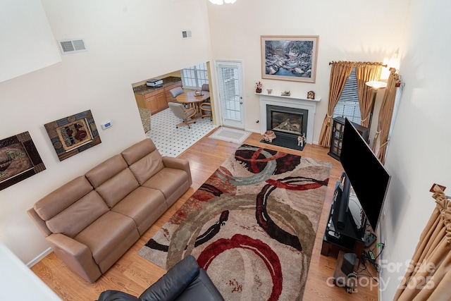 living area featuring wood finished floors, a fireplace with flush hearth, a high ceiling, and baseboards