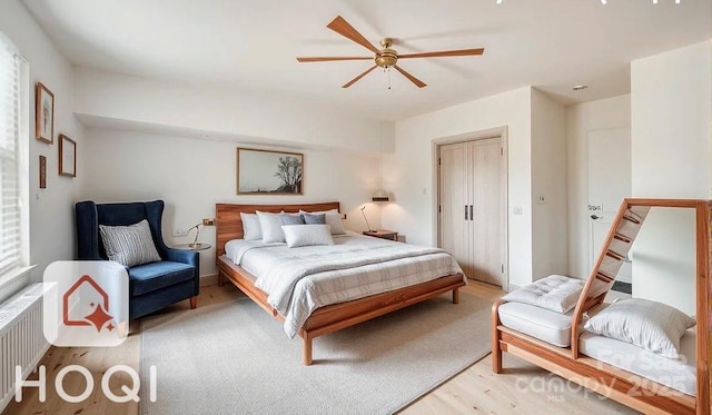 bedroom with light wood-style flooring, radiator heating unit, a ceiling fan, and a closet