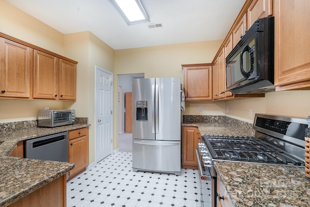 kitchen with stainless steel appliances, light floors, and dark stone counters