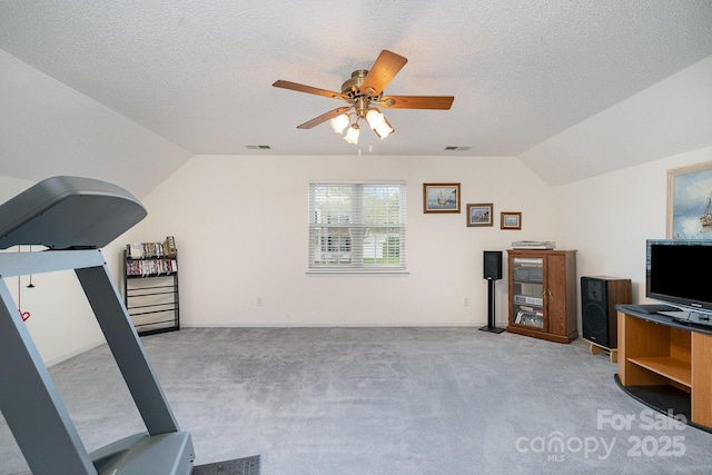 exercise room featuring ceiling fan, light colored carpet, vaulted ceiling, and a textured ceiling