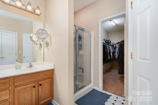 bathroom with a shower stall, vanity, a walk in closet, and baseboards