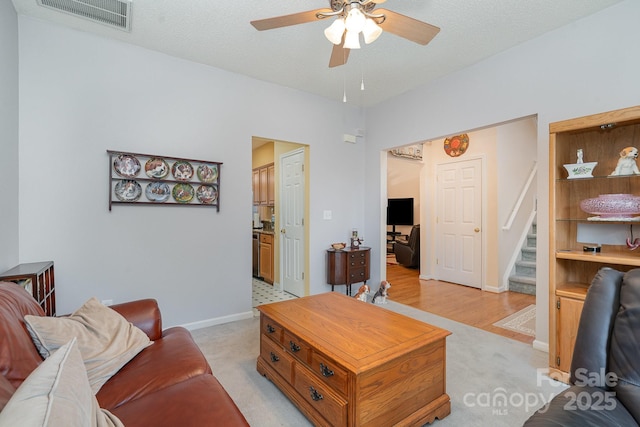 living area with ceiling fan, stairs, light colored carpet, and baseboards