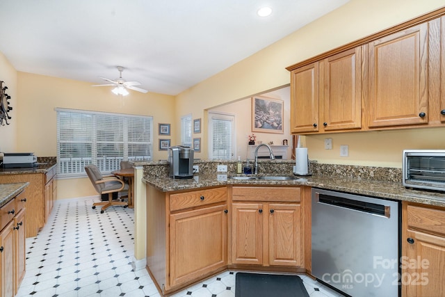 kitchen featuring dishwasher, a sink, a peninsula, ceiling fan, and dark stone counters