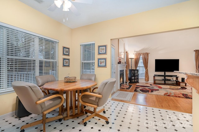 dining space featuring ceiling fan, a glass covered fireplace, tile patterned floors, and baseboards