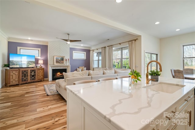 kitchen featuring light stone counters, a sink, a large fireplace, light wood-style flooring, and recessed lighting