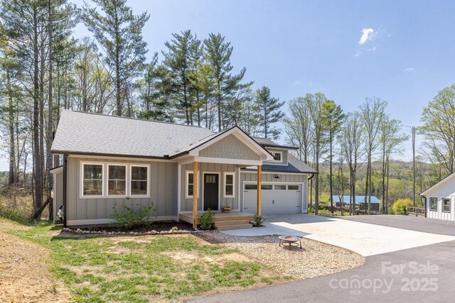209 Fall Leaves Dr, Fairview, NC 28730 - view of front of home featuring board and batten siding, driveway, a shingled roof, a fire pit, and a garage