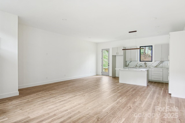 kitchen featuring backsplash, a kitchen island, light countertops, open floor plan, and light wood-style flooring