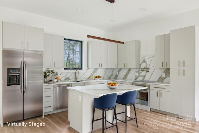 kitchen featuring a breakfast bar area, tasteful backsplash, a sink, light wood-style flooring, and appliances with stainless steel finishes