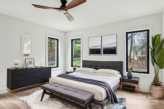 bedroom featuring baseboards, multiple windows, ceiling fan, and light wood-style floors