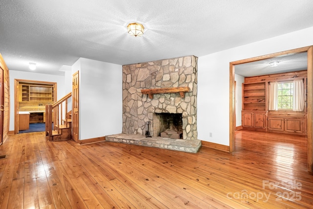 unfurnished living room with a textured ceiling, baseboards, wood-type flooring, and stairway