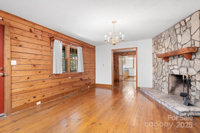 unfurnished living room with light wood-style flooring, a chandelier, baseboards, and a textured ceiling