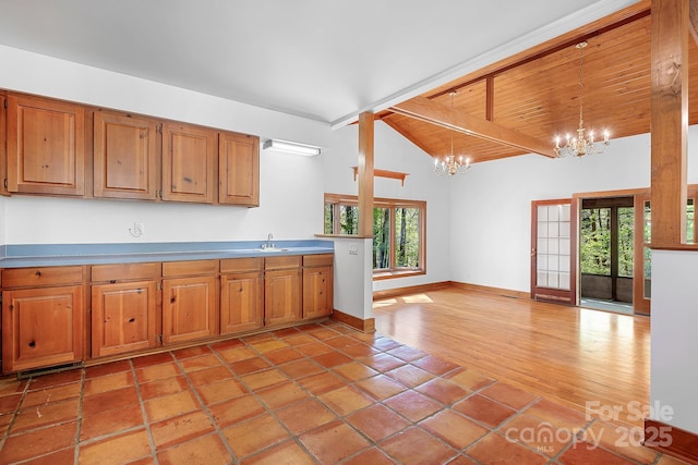 kitchen with decorative light fixtures, lofted ceiling with beams, a sink, a chandelier, and brown cabinetry