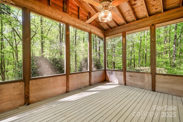 unfurnished sunroom featuring a wooded view and a ceiling fan
