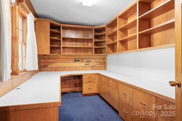 unfurnished office with a textured ceiling, dark colored carpet, and built in study area