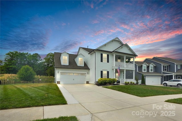 view of front of home with fence, an attached garage, a front lawn, a balcony, and driveway