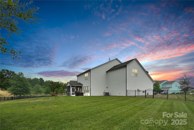 back of property at dusk with a sunroom, central AC unit, fence, and a yard